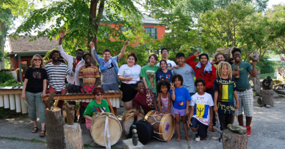 A large group of BIPOC teens outside with drums. 
