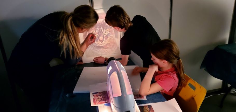 An adult and two children work on a painting of a cat.