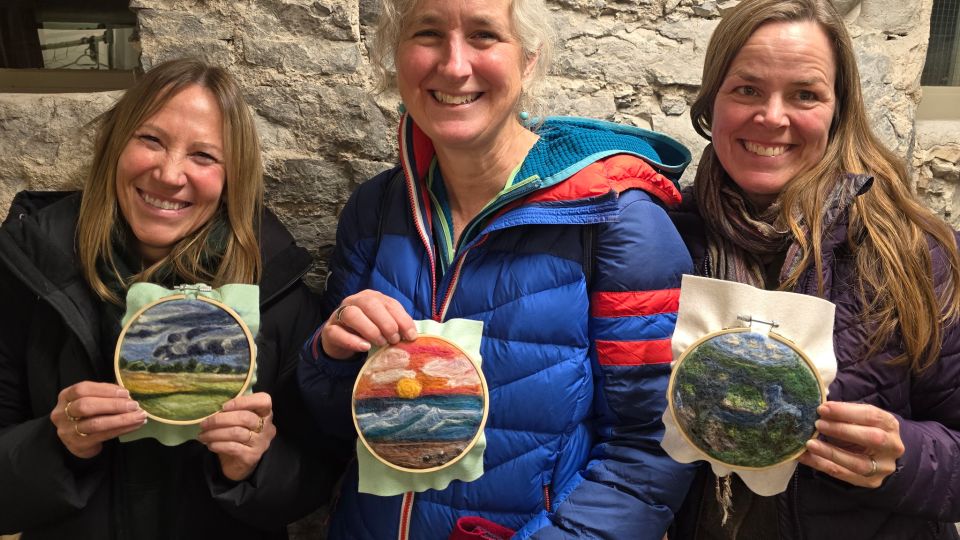 Three women show off their felted landscapes to the camera while smiling.