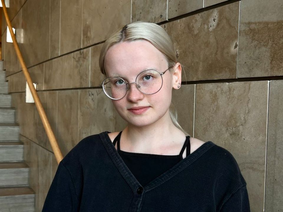 Photo of Emma in front of a staircase and beige tiled wall.