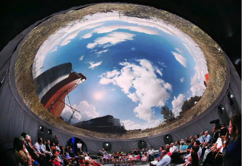 People seated in a round tent, looking at a projected image of the sky above them.